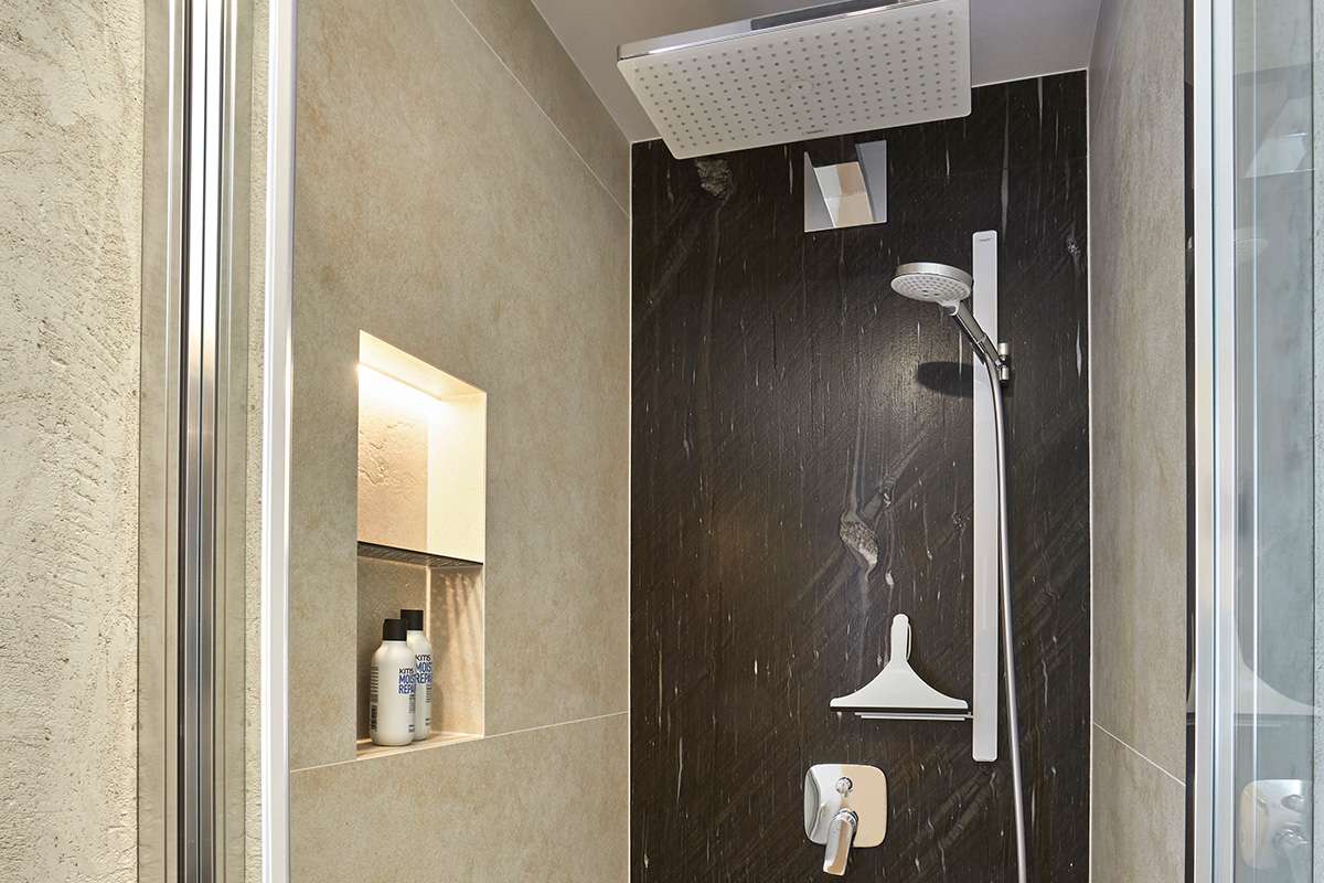 Traumbad mit Naturstein und großformatigen Fliesen Blick in Dusche mit Natursteinfliesen, mit Regendusche und praktischer Ablage in der Wand