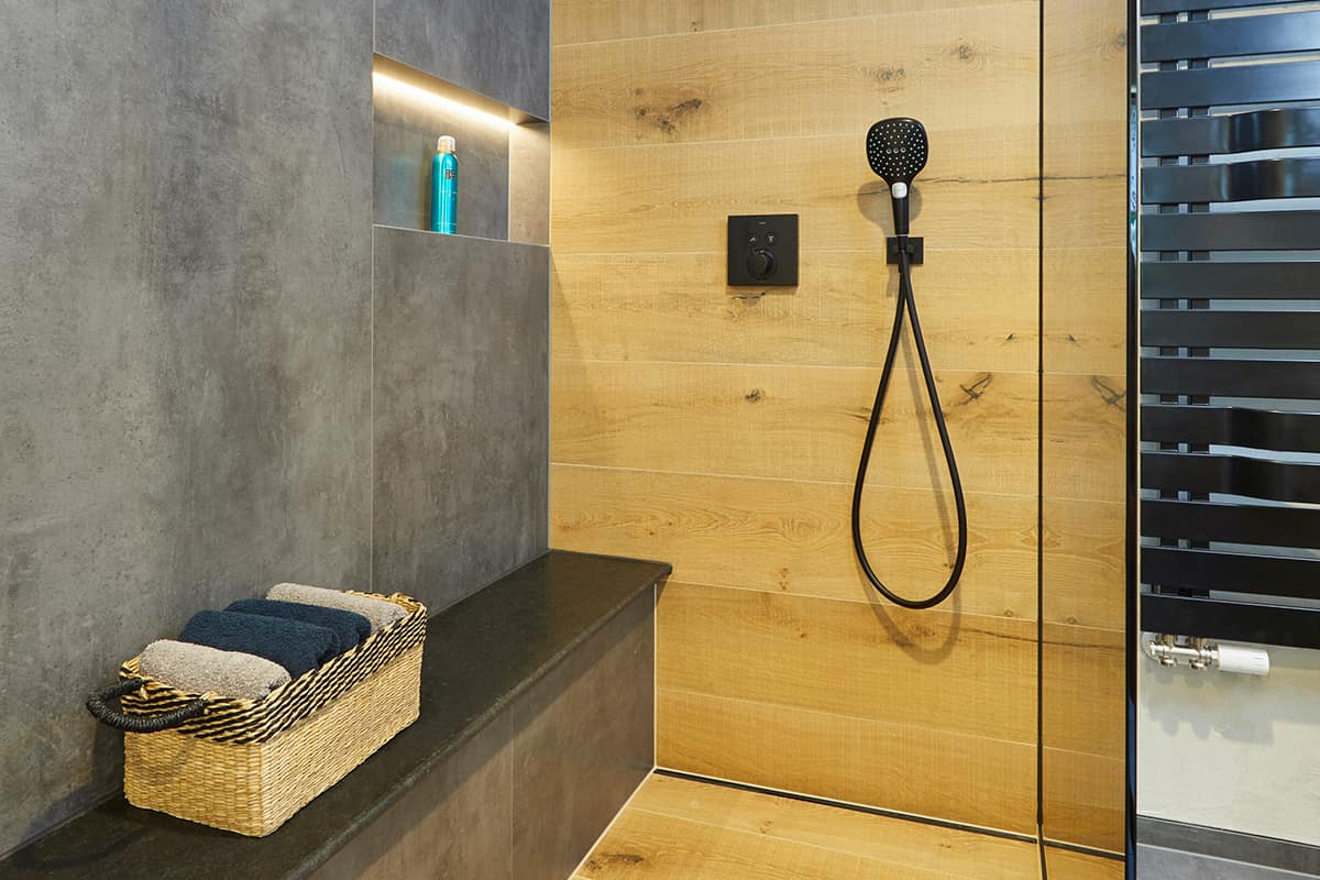 Wohlfühlbad mit Fliesen in Beton- & Holzoptik, Natursteinelementen & Dekorputz Blick auf Duschbereich mit Sitzmöglichkeit